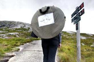 Hiker with tent in front of a signpost climbing Kjerag near Lysefjord, Kjerag, Rogaland, Norway