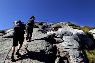 Hikers climbing Kjerag with safety chain and blue sky, Lysefjord, Rogaland, Norway