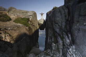Individual posing on floating rock with arms spread out, Lysefjord, Rogaland, Norway