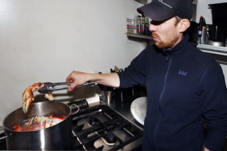 Man cooks king crab in a large cooking pot in the kitchen, Sarnes, Norway