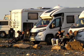 Campers relax next to motorhomes in a parking lot on the North Cape in the evening sun, North Cape,