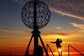Person jumping on the North Cape globe in front of a breathtaking sunset, North Cape, Magerøya,