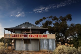 Dilapidated Lake Eyre Yacht Club building with eye-catching sign and trees, Marree, South