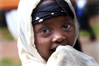 A child looks curiously at the camera, wrapped in a traditional headscarf, Key Afar, Basketo,