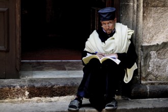 A priest sits reading on the steps of the Trinity Church in Addis Ababa, Addis Ababa, Ethiopia
