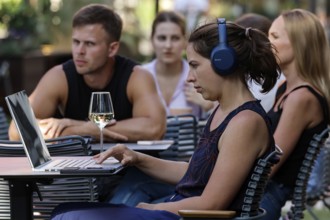 People relax in an outdoor cafe. A woman with laptop wearing headphones, Tallinn, Harju, Estonia