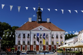 Impressive Tartu City Hall with red roof and flags on lively Town Hall Square, Rathausplatz,