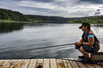 Young fisherman on a jetty on peaceful Ilgis Lake, surrounded by forest in Iginalina, Ignalina,
