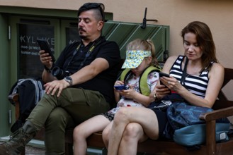 Family sitting on a bench in Tallinn's old town and is engrossed in their cellphones, Tallinn,