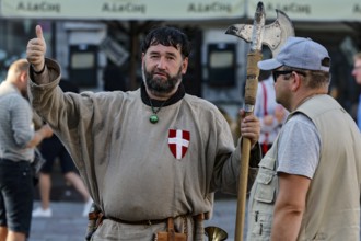 Two men, one in medieval traditional costume with an axe, on a busy square in Tallinn, Tallinn,
