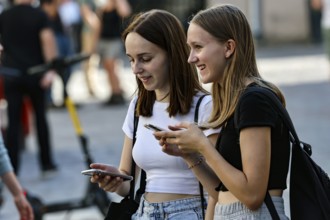 Two young woman laugh together while using their cell phones on the street, Tallinn, Harju, Estonia