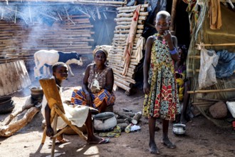 Women and children in the village, a woman preparing a meal surrounded by smoke and traditional