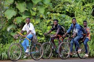 Four young people laugh on bicycles through a green, wooded area, Brobo, Côte d'Ivoire
