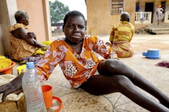 Woman sitting relaxing outdoors surrounded by water bottles, Bouké, region, Côte d'Ivoire