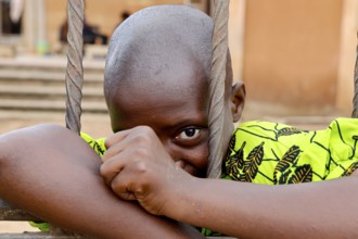 A child looks through metal mesh, a soft smile on his face, Bouké, region, Côte d'Ivoire