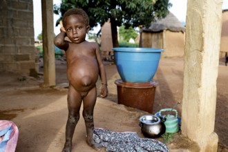 Child standing in front of simple dwellings in a rural village, Nionfouin, zero, Côte d'Ivoire