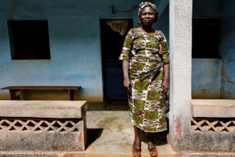 Kinafou stands in front of her house wearing traditional clothes, showing her cultural identity,