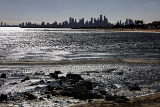 Melbourne skyline seen from Brighton Beach with reflecting sun rays on the water's edge, Brighton