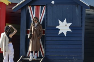 Beach visitors in front of a colorful beach house with flag motif in Brighton Beach, Brighton