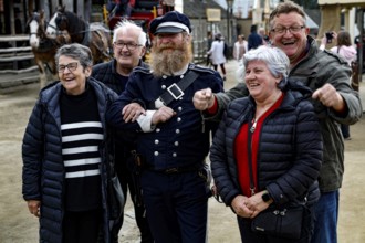 A performer in uniform stands smiling with a group of tourists for photos, Ballarat, Australia