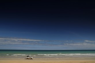 Vehicle on quiet shore of Cable Beach with clear, wide skies, Broome, Western Australia, Australia
