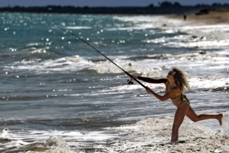 Female fisherman throws her fishing rod into the waves on Cable Beach, Broome, Western Australia,