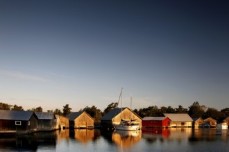 In Käringsund, colorful boathouses are reflected in the water under a clear evening sky,