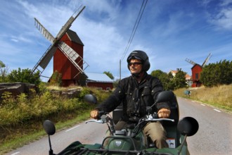 Man riding on ATV along a road with distinctive windmills, Långnäs, Åland, Finland