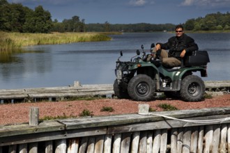 Man on ATV on lakeside with wooden walkway and quiet atmosphere, Lumpo, Åland, Finland