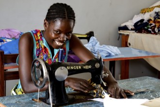 Woman working smiling on a sewing machine in a colorful sewing room, Bouaké, null, Côte d'Ivoire