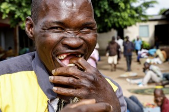 Laughing patient bites into food surrounded by other patients, Bouaké, Nimbo, Côte d'Ivoire