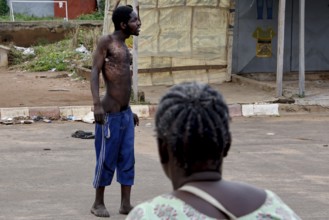 Mentally ill homeless person stands in the street while a woman sits nearby, Bouaké, Côte d'Ivoire