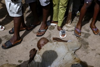 A homeless man lies asleep in the street surrounded by people, CI Bouaké, Ivory Coast