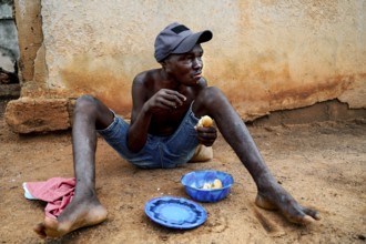 A laughing patient sits outside with plates in front of a wall, Bouaké, Nimbo, Côte d'Ivoire