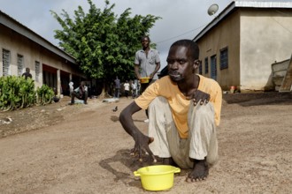 A patient sits with a bucket in the courtyard of a male psychiatric ward, Bouaké, Nimbo, Côte