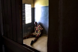 A man sits alone in a room at Saint Camille men's psychiatry, Bouaké, Côte d'Ivoire