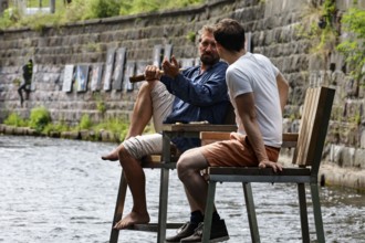 Two men sitting on high chairs in Vilnia river enjoying the ambiance, Vilnius, Uzupis, Lithuania