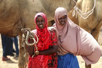Two woman with friendly smiles at the camel market in Babile, with camel in the background, Babile,