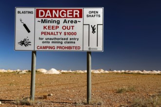 Warning sign of an opal mine in Coober Pedy with safety instructions in an arid desert landscape,