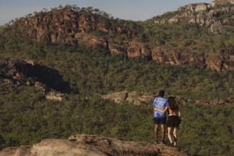 Two people on a rock with a view of wooded rocky landscape, Nawurlandia, Northern Territory,