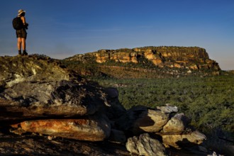 Tourist stands on a rocky plateau overlooking impressive rock walls in the evening sun,