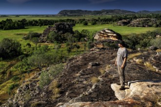 Person standing on a rocky outcrop with a wide view of green countryside, Ubirr, Northern