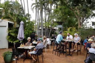 People eat and relax in Chinatown open-air café surrounded by palm trees, Broome, Western
