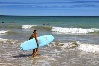 Surfer with blue surfboard standing on the water of Cable Beach, Broome, Western Australia,