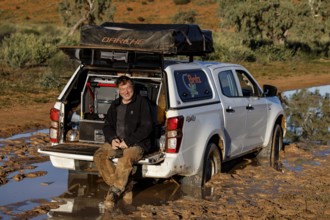 Man sits relaxed in the open trunk of a muddy off-road car on the Old Andado Track
