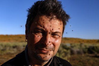 Portrait of a man surrounded by flies in a steppe-like landscape under clear sky, zero