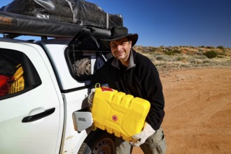 Person refuels vehicle with canister in the desert-like Simpson Desert, Simpson Desert, Australia