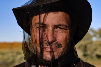 Man with a fly net over his face in front of a clear sky