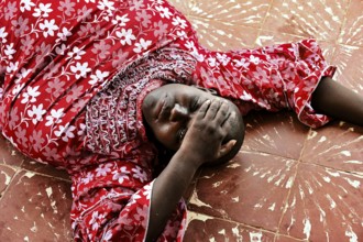 Woman wearing a red floral blouse lying relaxed on a patterned floor, Korhogo, null, Côte d'Ivoire