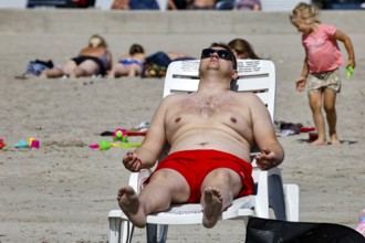 A man wearing red swimming trunks is relaxing on a lounger on a sandy beach, Pärnu, Estonia